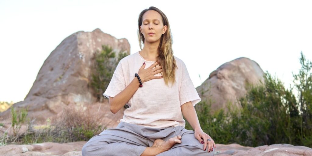 Person practicing yoga by the Ganga river, participating in guided meditation, and enjoying herbal tea in a serene natural setting.