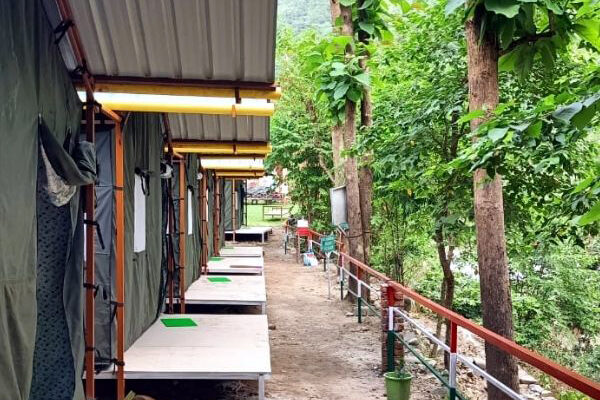 Riverside camping setup in Rishikesh with luxury tents, bonfire, and scenic mountain backdrop offering adventure activities and nature experiences.