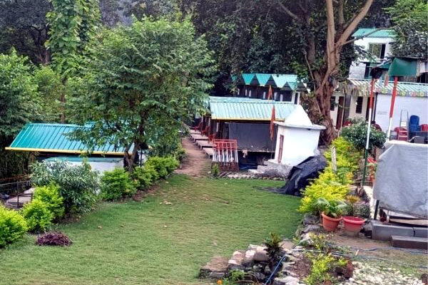 Riverside camping setup in Rishikesh with luxury tents, bonfire, and scenic mountain backdrop offering adventure activities and nature experiences.