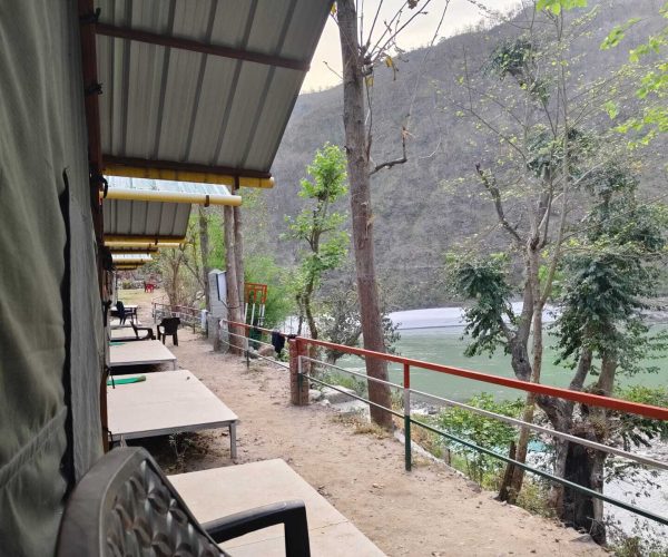 Cozy riverside camping tents set along the Ganga in Rishikesh, surrounded by mountains, offering bonfire nights and adventure activities.